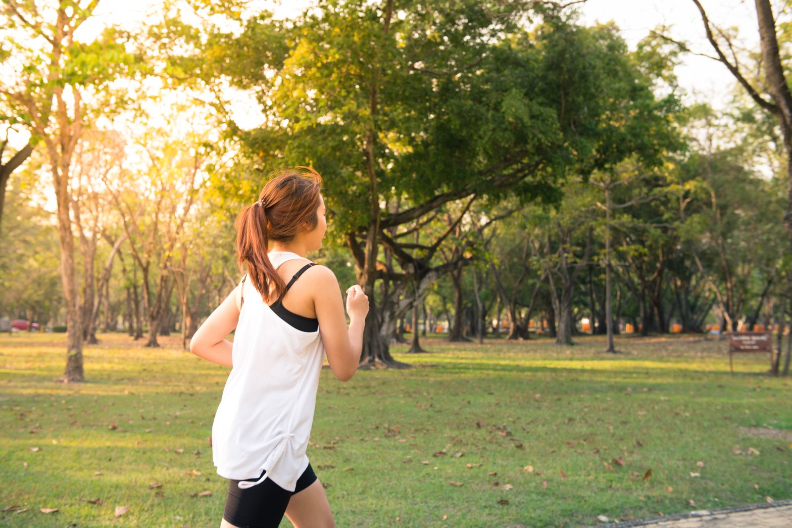 A woman running through woodland in early-morning golden light.