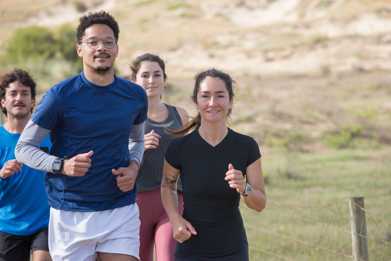 A diverse group of people running together outdoors on a bright day.