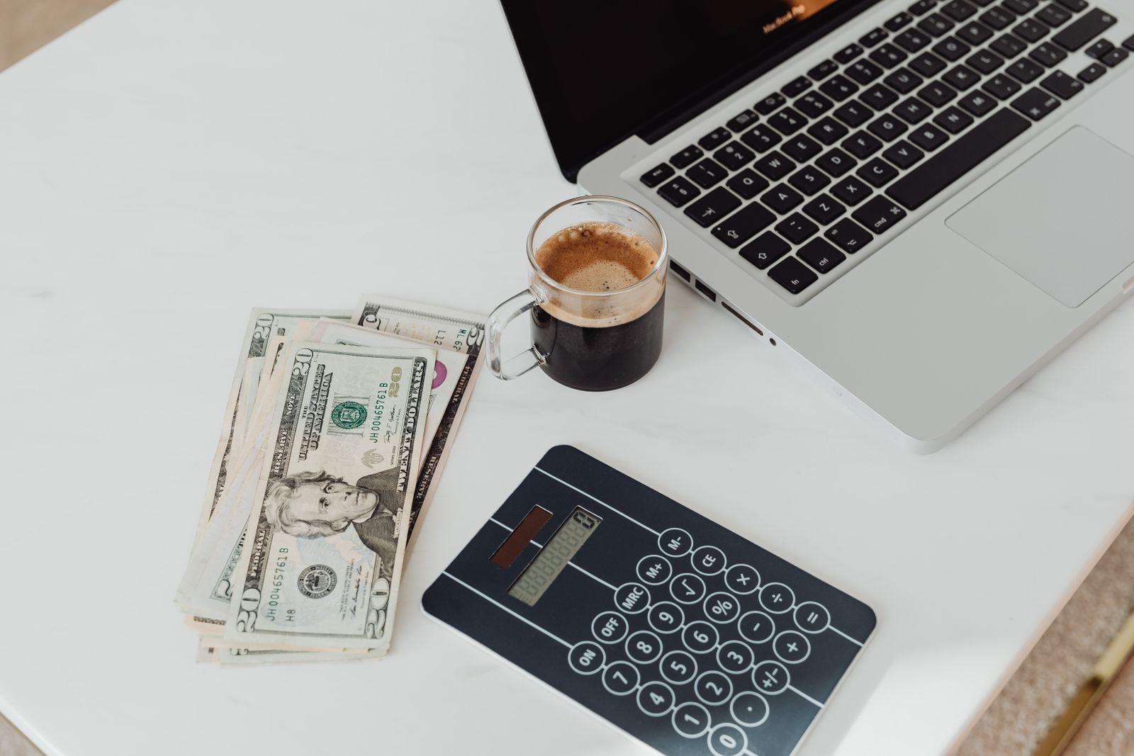 A calculator, cash and a laptop on a desk, mid-budgeting.