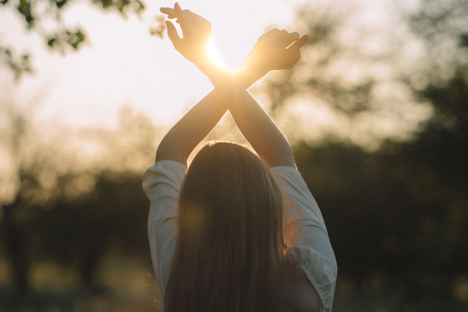 A woman stretching her arms towards the rising sun in a meadow.